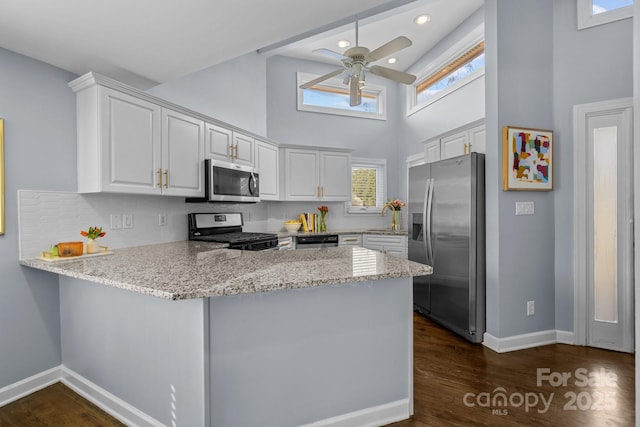 kitchen featuring light stone counters, dark wood-style floors, a peninsula, appliances with stainless steel finishes, and white cabinetry