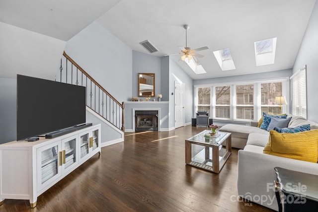 living area featuring stairway, wood finished floors, visible vents, vaulted ceiling with skylight, and ceiling fan