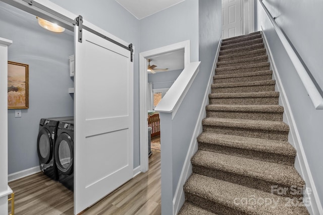 staircase with a ceiling fan, wood finished floors, washing machine and dryer, a barn door, and baseboards