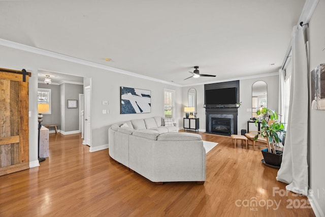 living room with a glass covered fireplace, a ceiling fan, a barn door, and wood finished floors