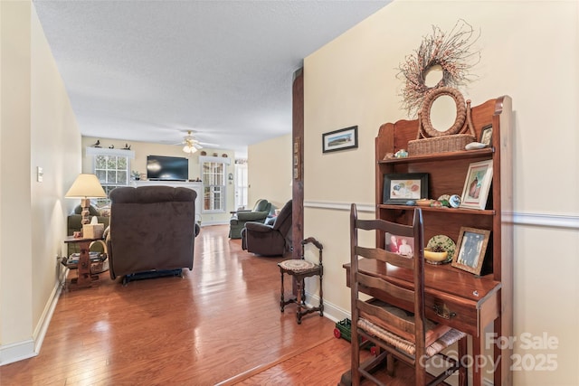 interior space with baseboards, a textured ceiling, ceiling fan, and wood finished floors