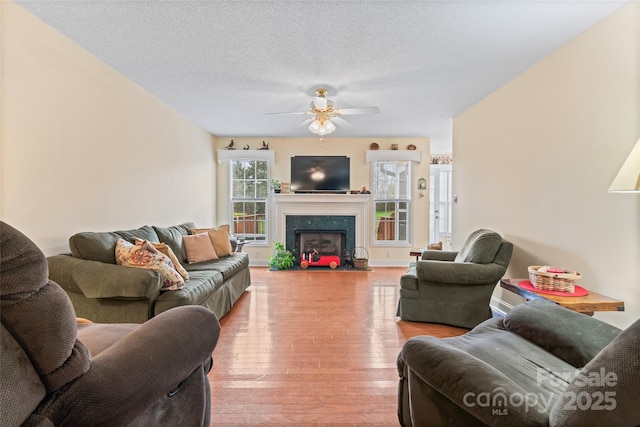 living room with a ceiling fan, baseboards, a premium fireplace, a textured ceiling, and light wood-type flooring