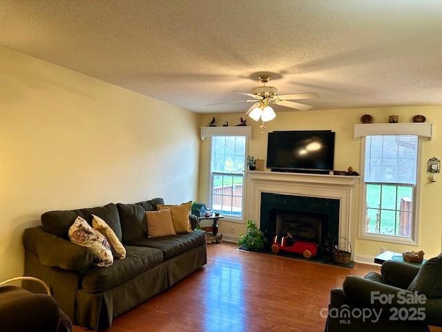 living area with a fireplace with raised hearth, a textured ceiling, ceiling fan, and wood finished floors