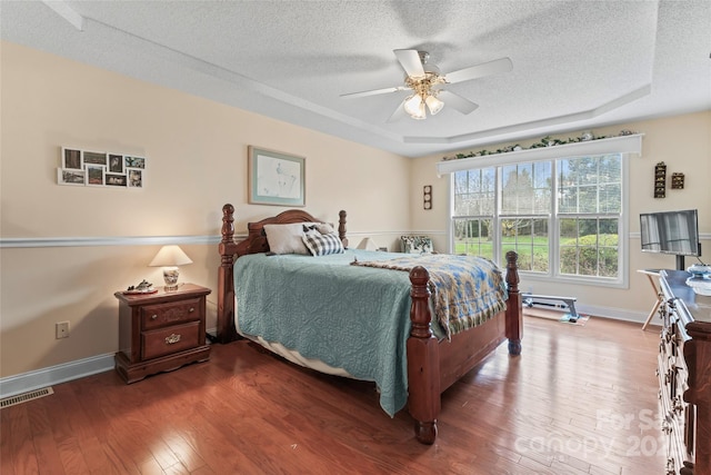 bedroom with a raised ceiling, visible vents, wood-type flooring, and a textured ceiling