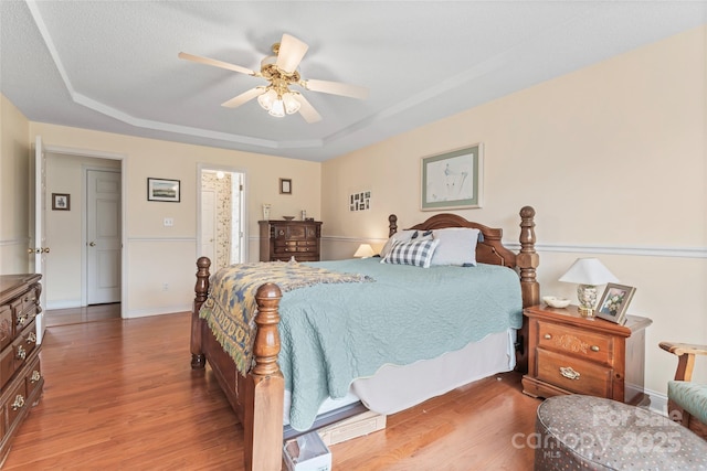 bedroom with a raised ceiling, wood finished floors, baseboards, and ceiling fan