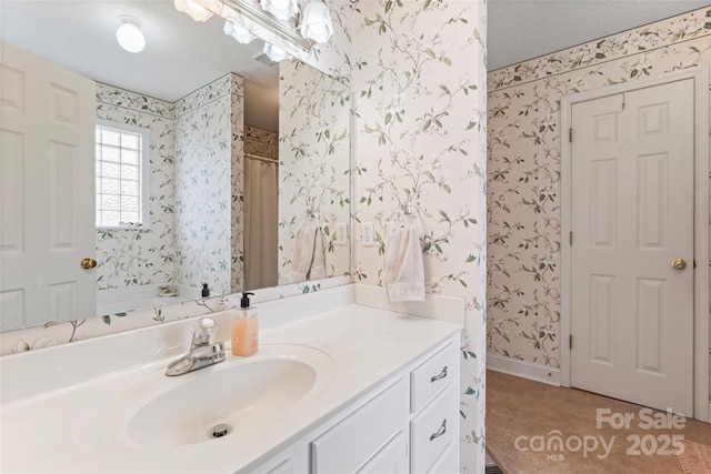 bathroom featuring a textured ceiling, wallpapered walls, vanity, and baseboards