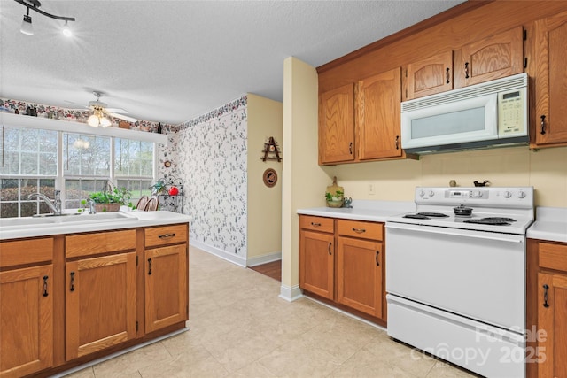 kitchen with a ceiling fan, a sink, a textured ceiling, white appliances, and wallpapered walls