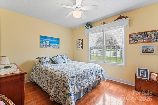 bedroom featuring baseboards, a textured ceiling, wood finished floors, and a ceiling fan