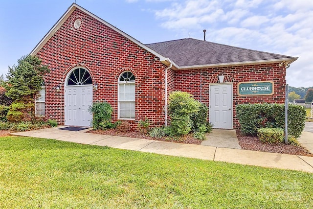 view of front facade with brick siding, a front yard, and a shingled roof