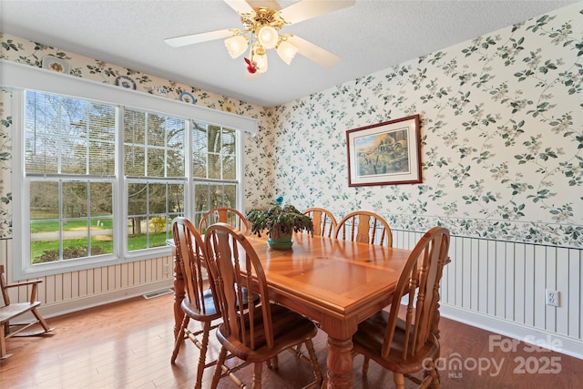 dining space featuring visible vents, a textured ceiling, wallpapered walls, and wood finished floors