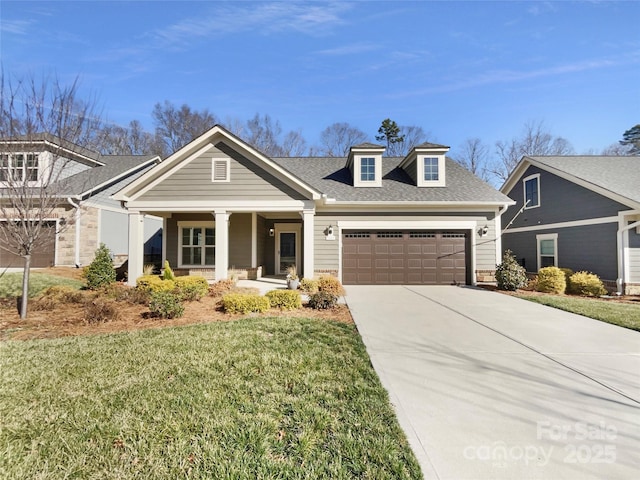 view of front of house with a front yard, driveway, roof with shingles, an attached garage, and covered porch