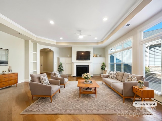 living room with ceiling fan, arched walkways, wood finished floors, and ornamental molding