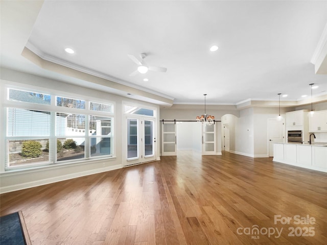 unfurnished living room with a ceiling fan, light wood-style flooring, arched walkways, a sink, and a barn door