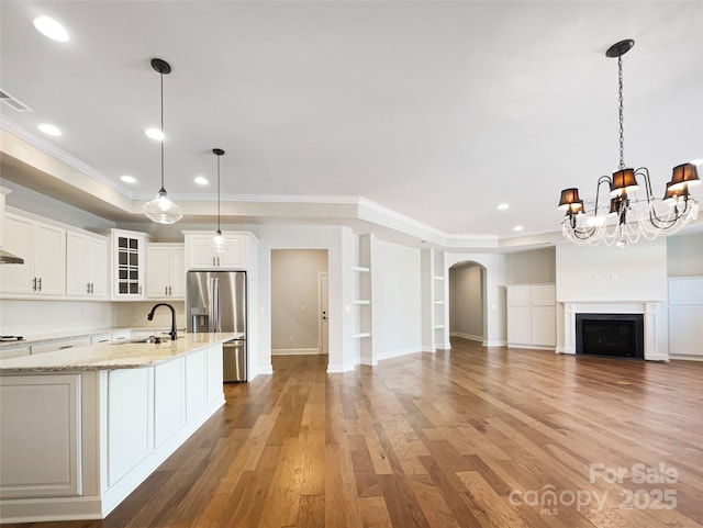 kitchen with an inviting chandelier, arched walkways, a sink, stainless steel refrigerator with ice dispenser, and light wood-type flooring