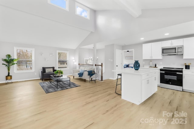 kitchen with a breakfast bar, electric stove, white cabinetry, stainless steel microwave, and a center island