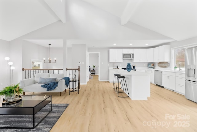 living area with beamed ceiling, a notable chandelier, light wood-style floors, and baseboards