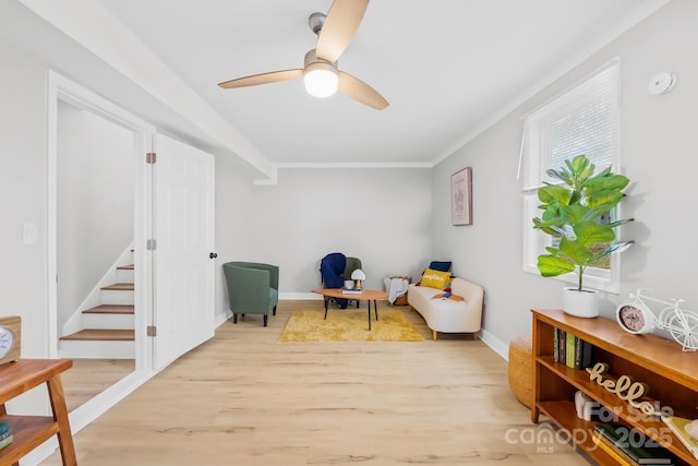 sitting room featuring light wood finished floors, crown molding, baseboards, stairway, and a ceiling fan