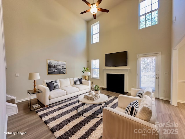 living area featuring a fireplace with flush hearth, wood finished floors, baseboards, and ceiling fan