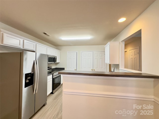 kitchen with visible vents, light wood-type flooring, dark countertops, white cabinetry, and appliances with stainless steel finishes