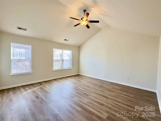 spare room featuring dark wood-type flooring, vaulted ceiling, visible vents, and ceiling fan