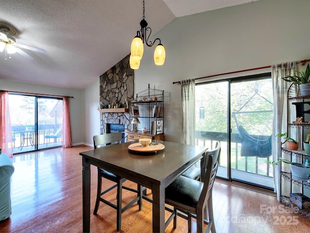 dining space featuring ceiling fan, lofted ceiling, a stone fireplace, wood finished floors, and a textured ceiling