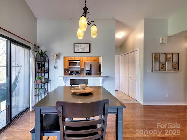 dining space featuring a high ceiling, baseboards, and light wood-type flooring