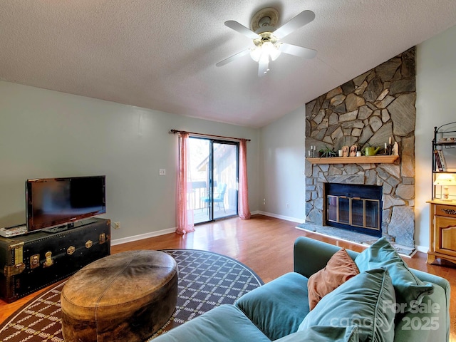 living area with a stone fireplace, wood finished floors, a ceiling fan, and vaulted ceiling