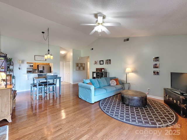 living area with visible vents, lofted ceiling, wood finished floors, a textured ceiling, and a ceiling fan