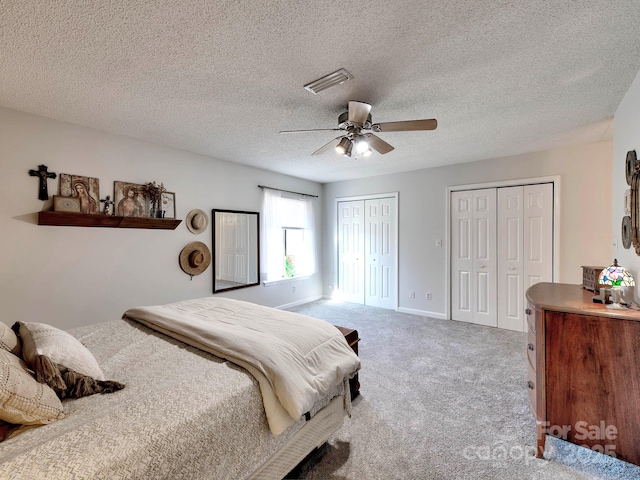 carpeted bedroom featuring visible vents, ceiling fan, baseboards, multiple closets, and a textured ceiling