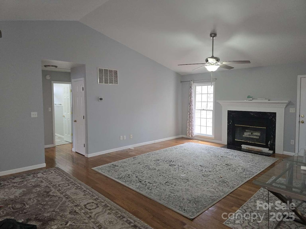 living area with wood finished floors, a ceiling fan, visible vents, lofted ceiling, and a high end fireplace