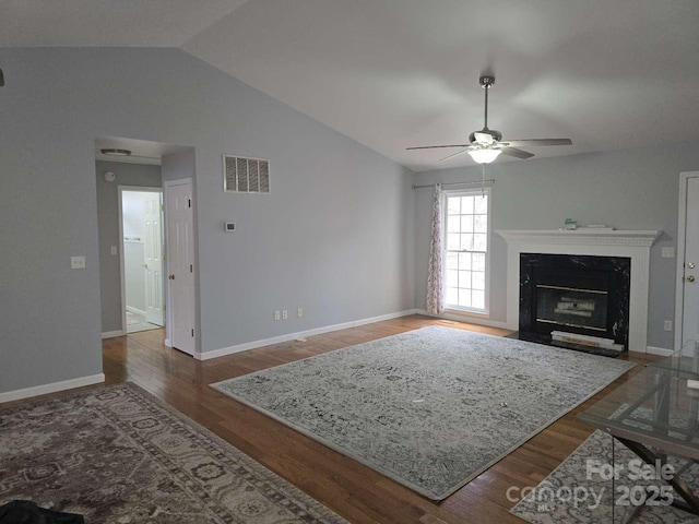 living area featuring visible vents, a ceiling fan, wood finished floors, a high end fireplace, and vaulted ceiling