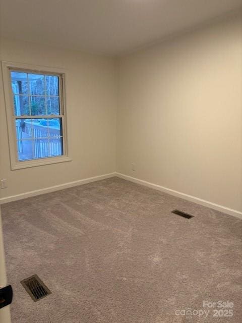 unfurnished room with visible vents, dark carpet, and baseboards