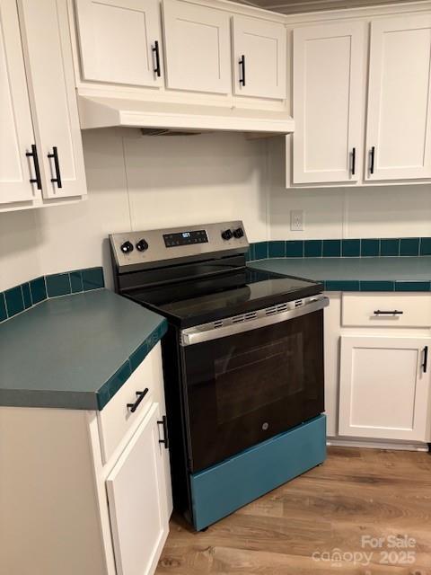 kitchen with dark countertops, electric range, and white cabinetry