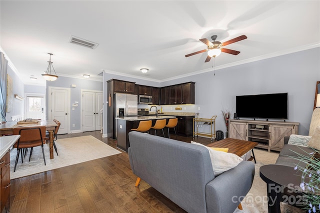 living area with ornamental molding, dark wood-style floors, visible vents, and ceiling fan