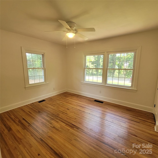 unfurnished room with a wealth of natural light, visible vents, wood finished floors, and a ceiling fan