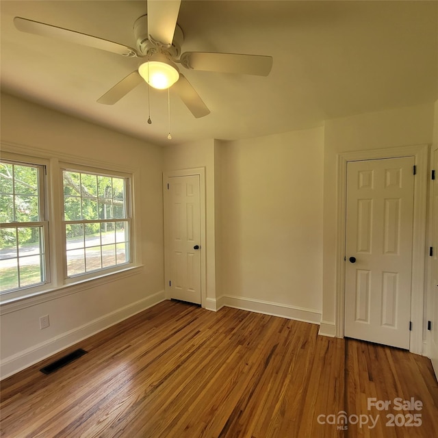 spare room with ceiling fan, visible vents, baseboards, and wood finished floors