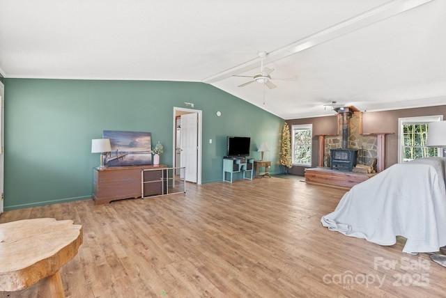 living area with wood finished floors, baseboards, a wood stove, ceiling fan, and vaulted ceiling