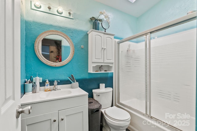 full bath with vanity, toilet, a textured wall, and combined bath / shower with glass door