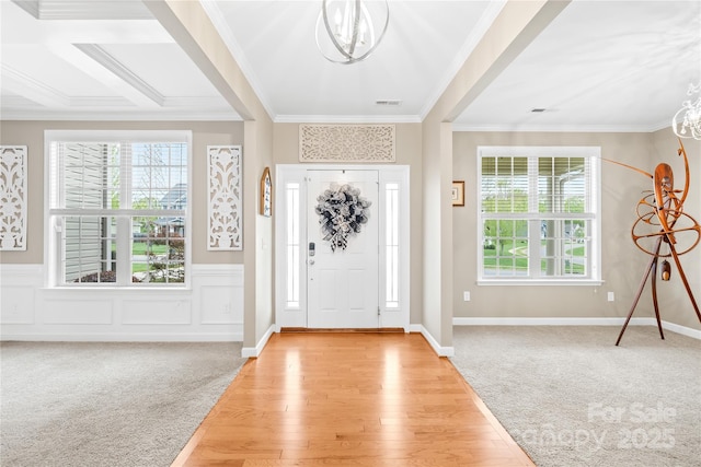 foyer featuring a chandelier, crown molding, light wood finished floors, wainscoting, and light colored carpet