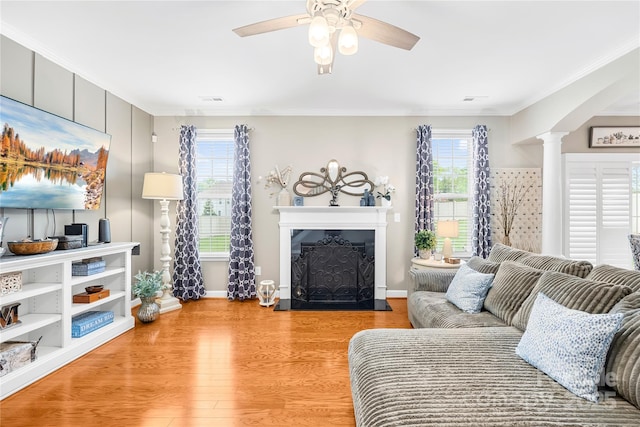 living area with visible vents, ornamental molding, a ceiling fan, a fireplace, and light wood-style flooring
