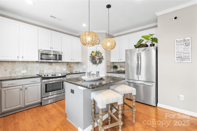kitchen with appliances with stainless steel finishes, light wood finished floors, visible vents, and a kitchen island