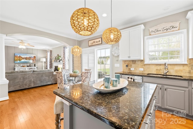 kitchen featuring open floor plan, crown molding, decorative light fixtures, arched walkways, and a sink
