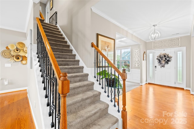 foyer entrance with wood finished floors, a notable chandelier, ornamental molding, and stairway