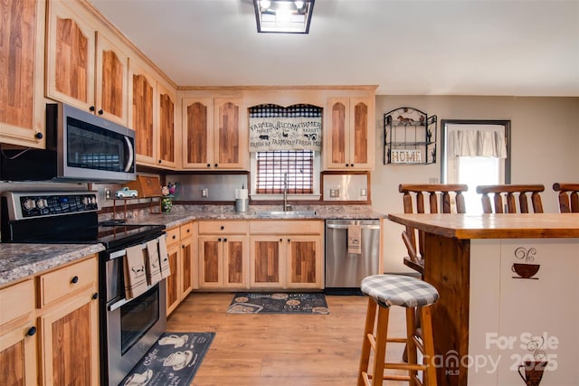 kitchen with a breakfast bar, light brown cabinets, a sink, stainless steel appliances, and light wood-style floors