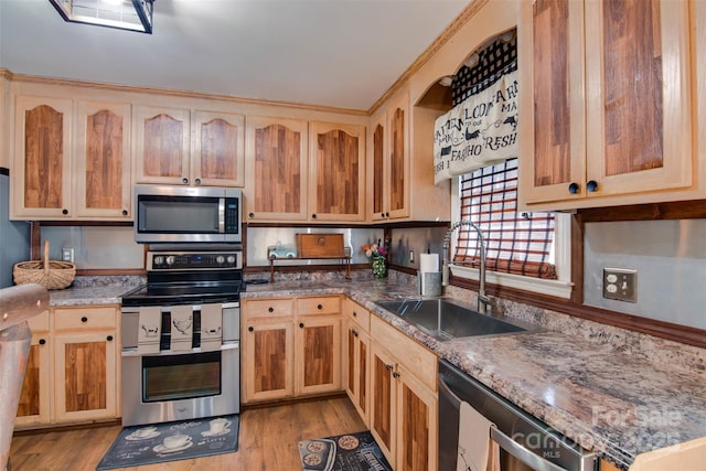 kitchen with light brown cabinets, light wood-style flooring, appliances with stainless steel finishes, stone countertops, and a sink