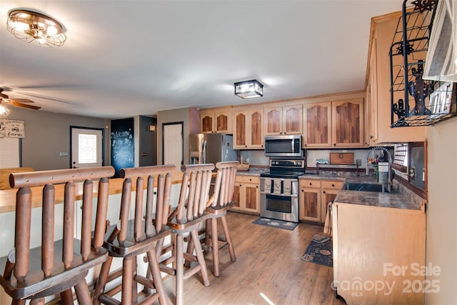 kitchen featuring dark countertops, light wood-style flooring, stainless steel appliances, a ceiling fan, and a sink