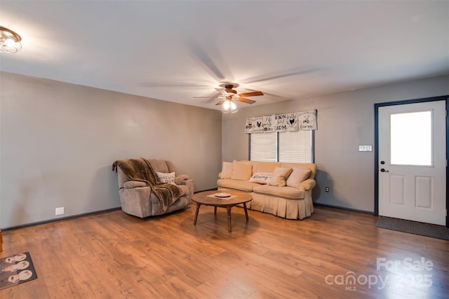 living area featuring baseboards, a ceiling fan, and wood finished floors