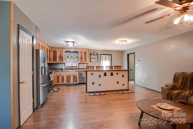 kitchen featuring wood finished floors, light brown cabinets, a sink, ceiling fan, and appliances with stainless steel finishes