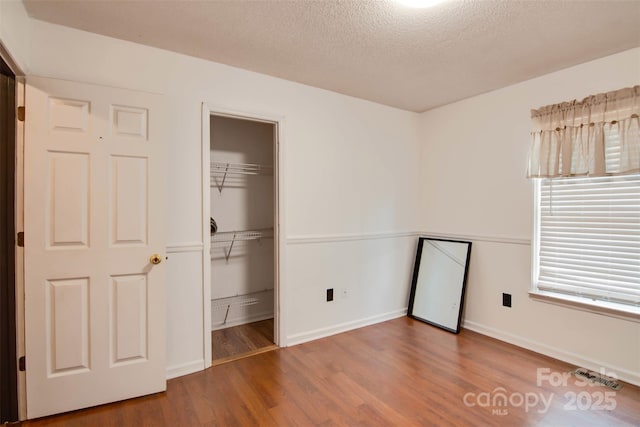 unfurnished bedroom featuring visible vents, a textured ceiling, baseboards, and wood finished floors