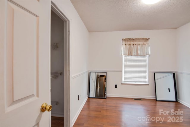 spare room featuring baseboards, wood finished floors, visible vents, and a textured ceiling